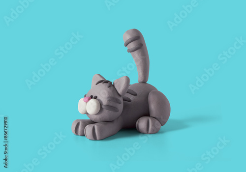 Cute lying cat handmade with gray plasticine on a blue background. Plasticine modeling of little cat. Clay farm animal