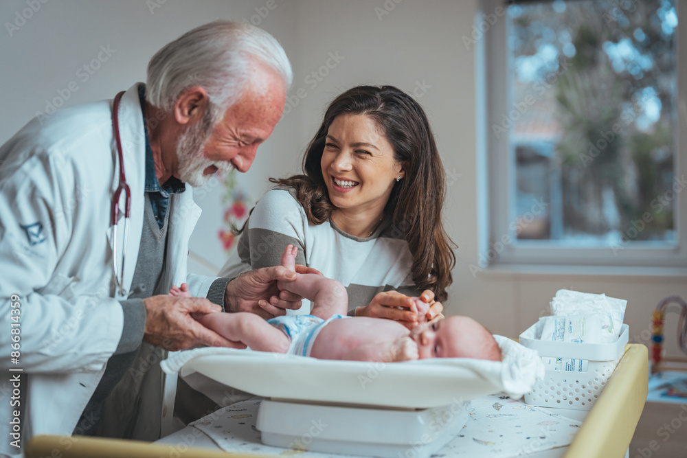 A smiling elderly male pediatrician in a white coat examines a baby with a joyful young adult female observing, in a well-equipped hospital room. A smiling elderly male pediatrician in a white coat examines a baby with a joyful young adult female observing, in a well-equipped hospital room.