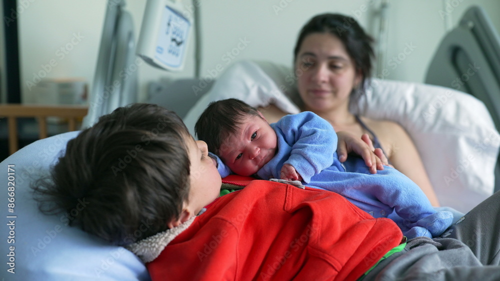 Newborn baby in blue onesie cuddling with older sibling, both resting on hospital bed, with mother watching lovingly in the background, capturing a warm and affectionate family moment Newborn baby in blue onesie cuddling with older sibling, both resting on hospital bed, with mother watching lovingly in the background, capturing a warm and affectionate family moment