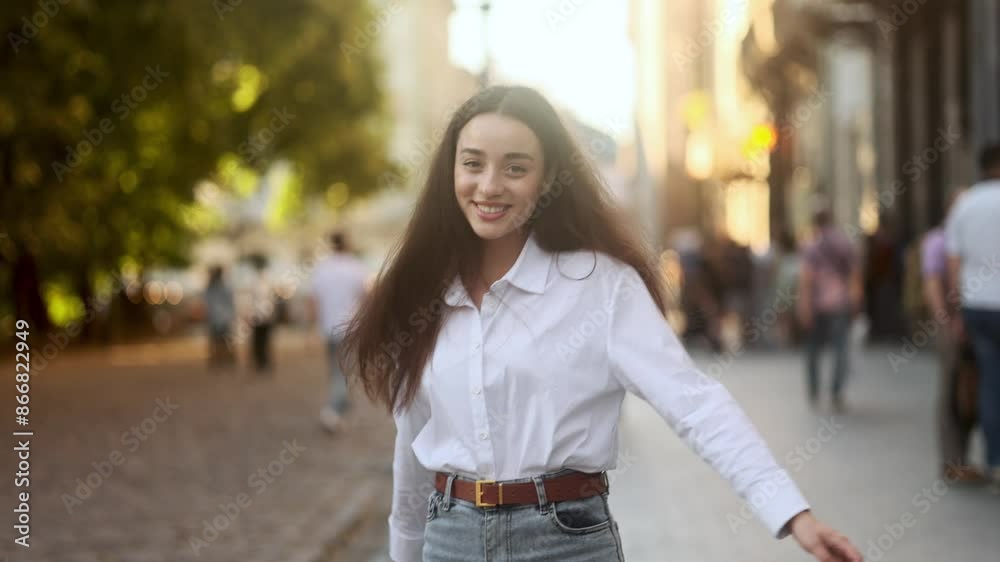 Charming young caucasian woman walking down the street turns around with flying hair and looking at camera outdoors Smiling female walking enjoying beautiful day in the city centre alone Charming young caucasian woman walking down the street turns around with flying hair and looking at camera outdoors Smiling female walking enjoying beautiful day in the city centre alone
