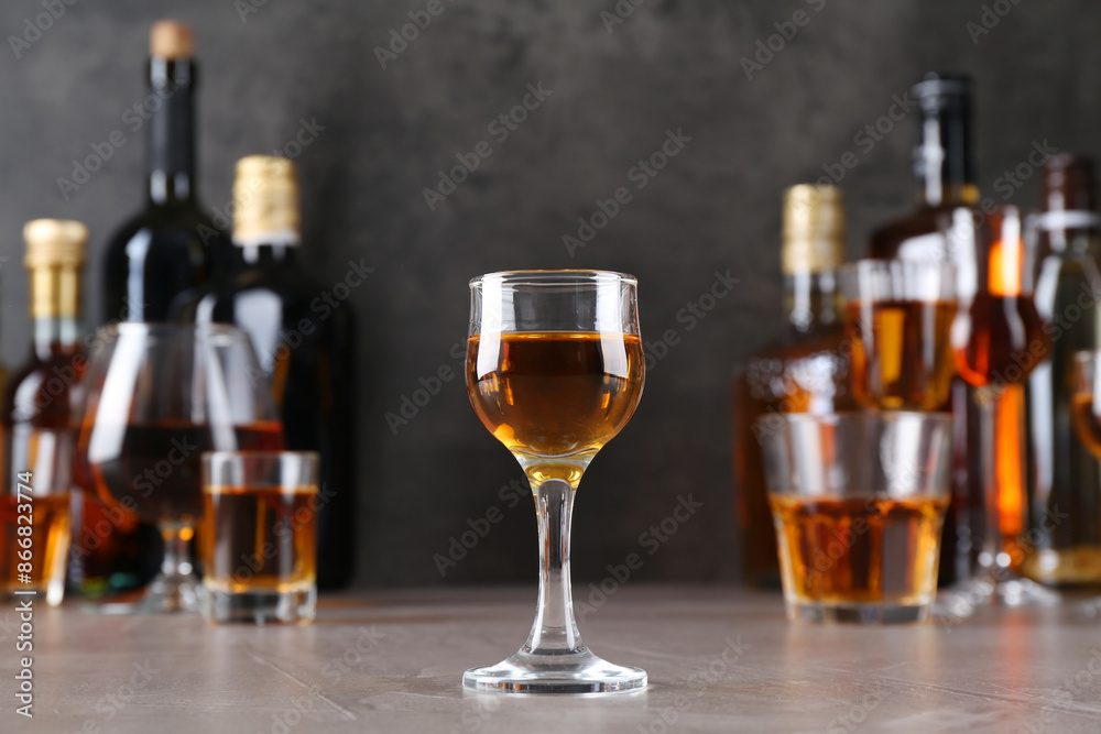 One liqueur in glass in front of others on grey textured table, closeup One liqueur in glass in front of others on grey textured table, closeup