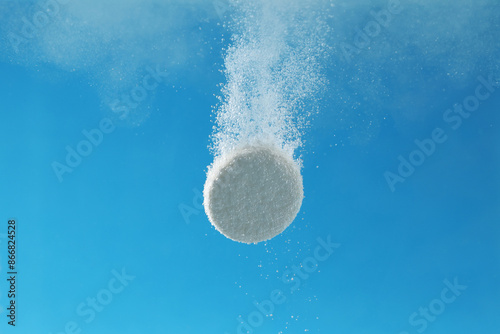 Effervescent pill dissolving in water on light blue background, closeup