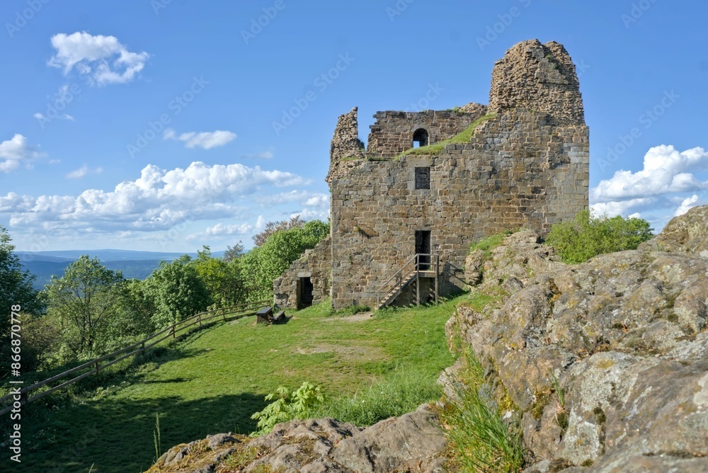 Hrad Přimda stands tall atop a hill, its ancient ruins glowing under a bright blue sky on a summer day. Hrad Přimda stands tall atop a hill, its ancient ruins glowing under a bright blue sky on a summer day.