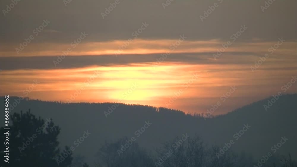 Misty view with sky during sunrise, moving fumes and orange clouds over dark horizon of Silesian Beskid mountains and trees in Poland on autumn heating season - timelapse.