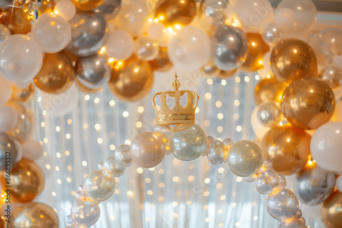 stunning glittery balloon arch in shades of gold, silver, and white, forming the perfect backdrop for a birthday party. At the center of the arch, a large golden crown adds a regal