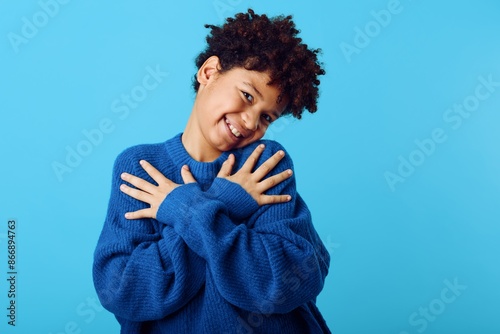 Beaming african american girl in cozy blue sweater radiates joy against a vibrant blue background