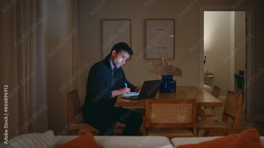 Busy professional working laptop at table home. Serious man writing notes late Busy professional working laptop at table home. Serious man writing notes late