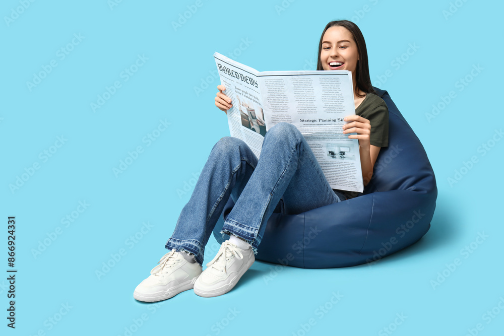 Beautiful young woman in beanbag chair with newspaper on blue background Beautiful young woman in beanbag chair with newspaper on blue background