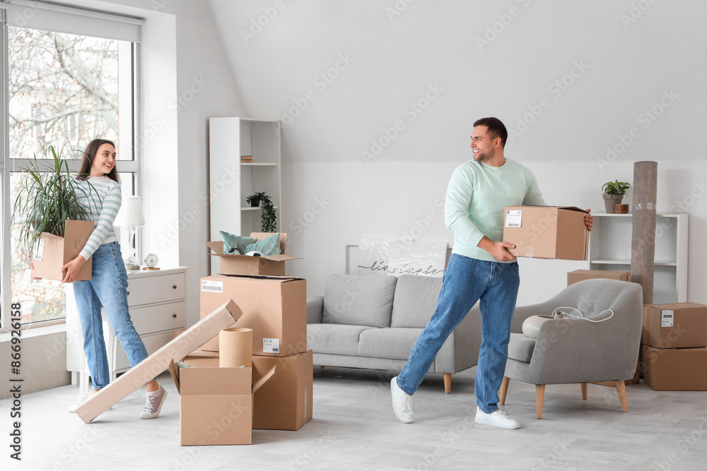 Happy young couple carrying boxes in room on moving day Happy young couple carrying boxes in room on moving day