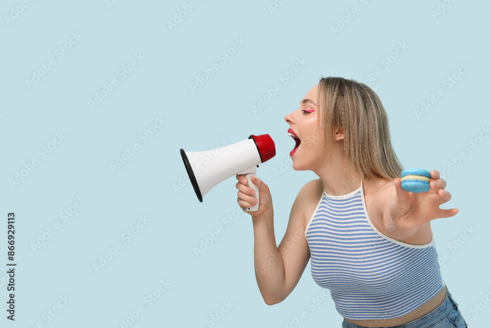 Beautiful young woman with sweet macaroon and loudhailer on blue background Beautiful young woman with sweet macaroon and loudhailer on blue background