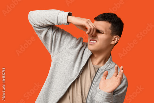 Handsome young man pinching nose because of bad smell on orange background photo