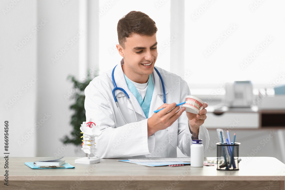 Young male dentist with jaw model at table in clinic Young male dentist with jaw model at table in clinic