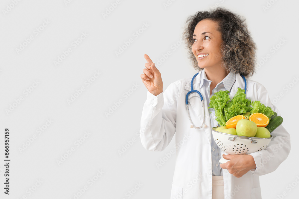 Mature female nutritionist with healthy food pointing at something on light background Mature female nutritionist with healthy food pointing at something on light background