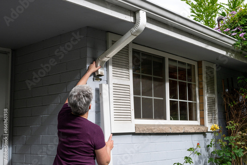 Middle aged white woman re-installing a rain gutter downspout after cleaning it out, homeowner maintenance
