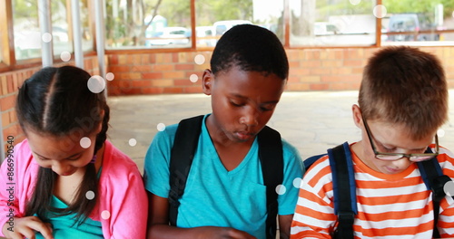 Image of floating dots over diverse girls and boys using digital tablet in classroom at school