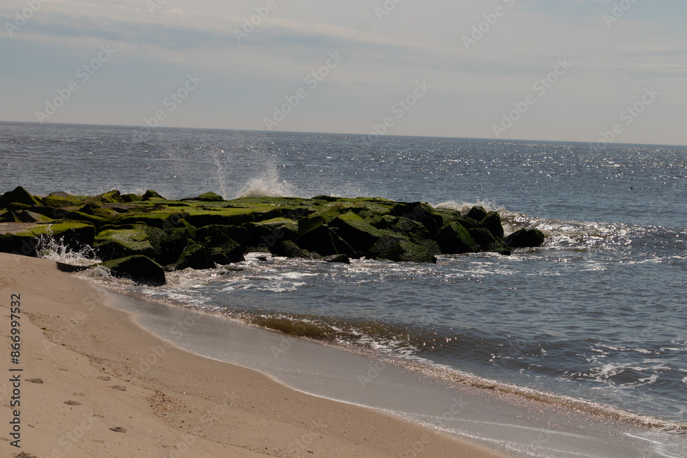 This is a picture of a jetty stretching out into the water. The waves crashing all around showing white froth. The large black rocks coming out of the bay with emerald green moss growing on them. This is a picture of a jetty stretching out into the water. The waves crashing all around showing white froth. The large black rocks coming out of the bay with emerald green moss growing on them.