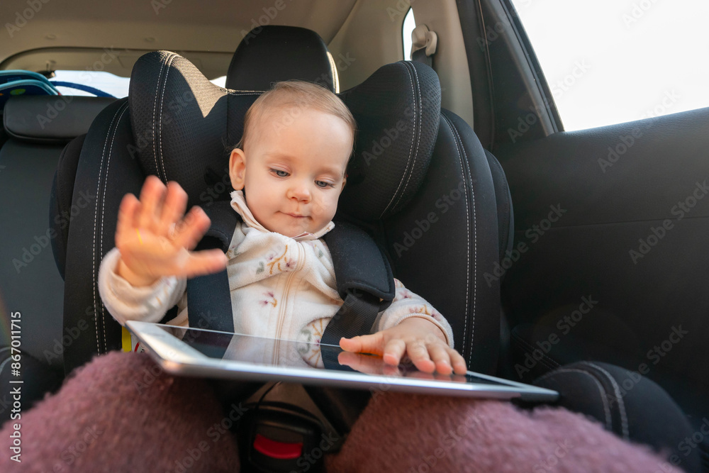 Small girl in child car seat using digital tablet on a road trip. Concept of kids travel safety and entertainment Small girl in child car seat using digital tablet on a road trip. Concept of kids travel safety and entertainment