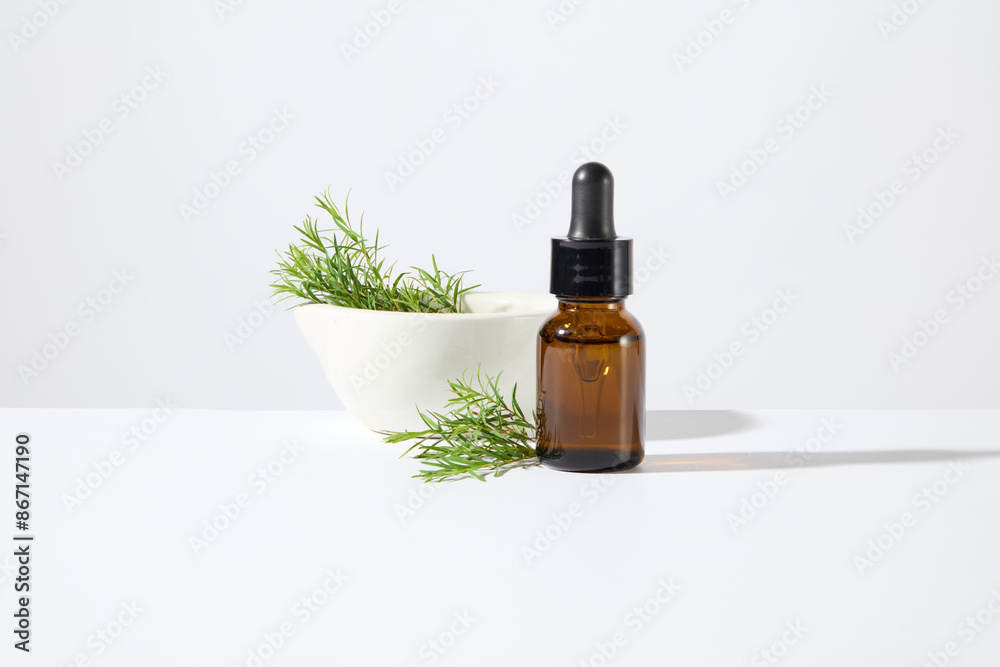 Front view template for cosmetic advertising poster with a brown color unlabeled serum bottle isolated on the white texture, beside it is a white ceramic bowl containing tea tree branches Front view template for cosmetic advertising poster with a brown color unlabeled serum bottle isolated on the white texture, beside it is a white ceramic bowl containing tea tree branches