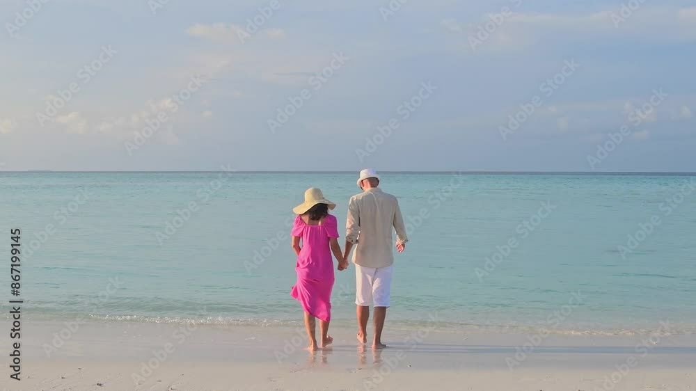 Beautiful tourist couple walks down a tropical beach with turquoise ocean and sunshine in the Maldives islands. Looking at each other and having fun. Romantic holidays vacation Beautiful tourist couple walks down a tropical beach with turquoise ocean and sunshine in the Maldives islands. Looking at each other and having fun. Romantic holidays vacation