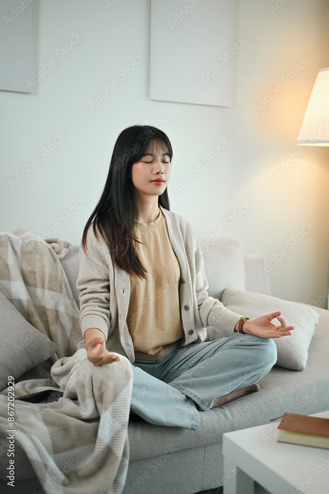 Portrait of beautiful young Asian woman meditating with closed eyes on sofa at home Portrait of beautiful young Asian woman meditating with closed eyes on sofa at home