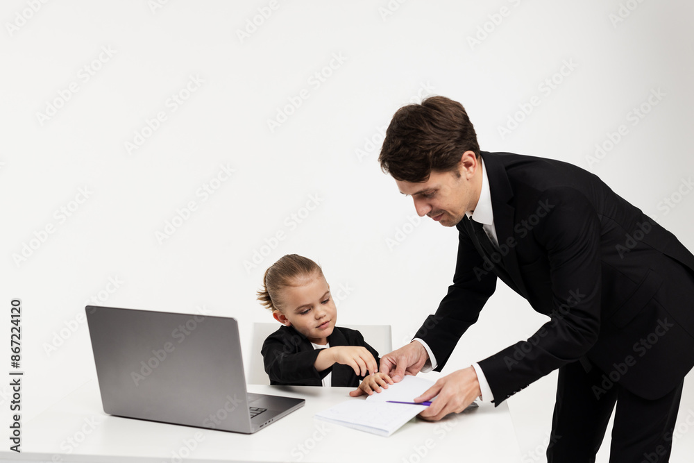 A little girl director in a business suit at an office table and a laptop talks with adult subordinates. Business and finance concept. A little girl director in a business suit at an office table and a laptop talks with adult subordinates. Business and finance concept.