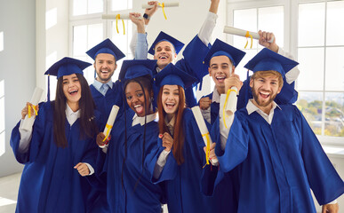 Group of excited smiling happy multiracial international graduates students having fun in a university graduate blue gown holding diploma indoors. Education and graduation concept.