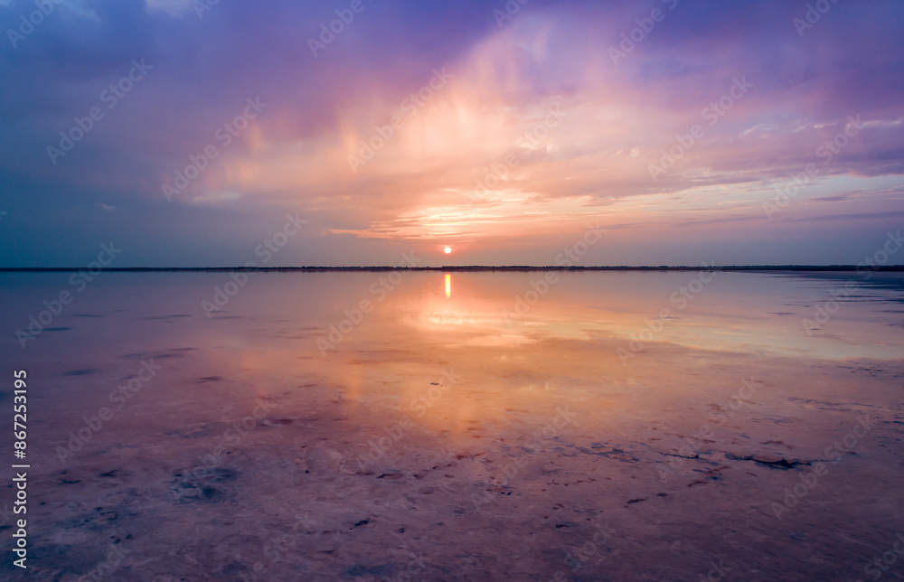 A serene sunset over Burlinskoe Lake, a salt lake located near Bursol. The sky is a beautiful mix of purple and orange hues, with the setting sun reflecting on the calm waters. A serene sunset over Burlinskoe Lake, a salt lake located near Bursol. The sky is a beautiful mix of purple and orange hues, with the setting sun reflecting on the calm waters.