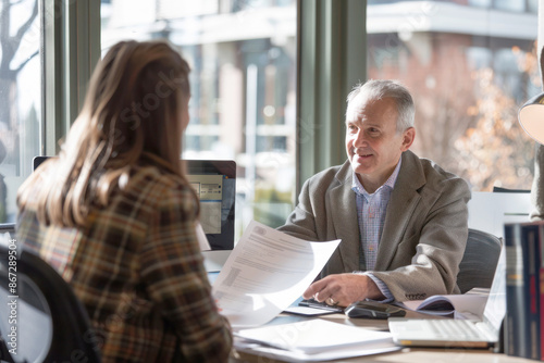 Tax Advisor Discussing Documents with Client in Office with Computer and Tax Books Under Natural Daylight