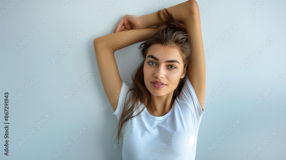 Confident young woman with arms raised, showing her armpits, in a white t-shirt against a light blue background, radiating natural beauty and ease Confident young woman with arms raised, showing her armpits, in a white t-shirt against a light blue background, radiating natural beauty and ease