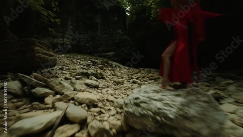 An Asian girl in a beautiful red kimono and a Vietnamese triangular hat is dancing sexually in nature in a rocky canyon