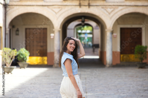 young and beautiful latin woman, walking down a central street in the city of Seville, the woman looks back and smiles while on holiday in Spain. Travel and holiday concept.
