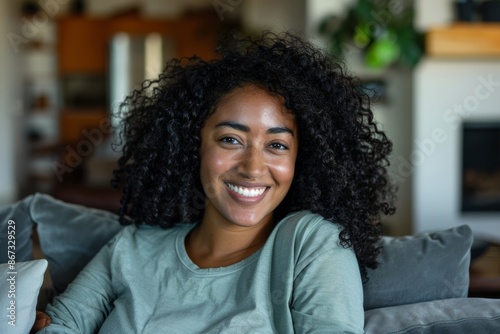 Naturally curly hair and broad, gorgeous grin, this beautiful African adolescent girl is posing indoors on a sofa Portrait of Generation Z. © MUNUGet Ewa