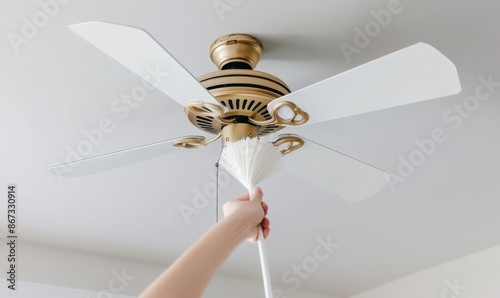 close-up of hand holding white brush cleaning ceiling fan, woman's hand using air duster cleaner and fresh spray to clean light lamp in room, detailed cleaning action photo