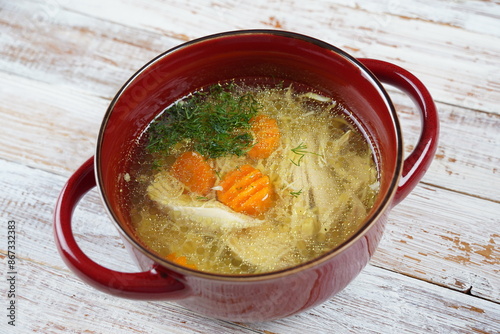 Chicken soup, chicken broth, with pieces of chicken and vegetables in red bowl with handles . Chicken bouillon, boiled meat