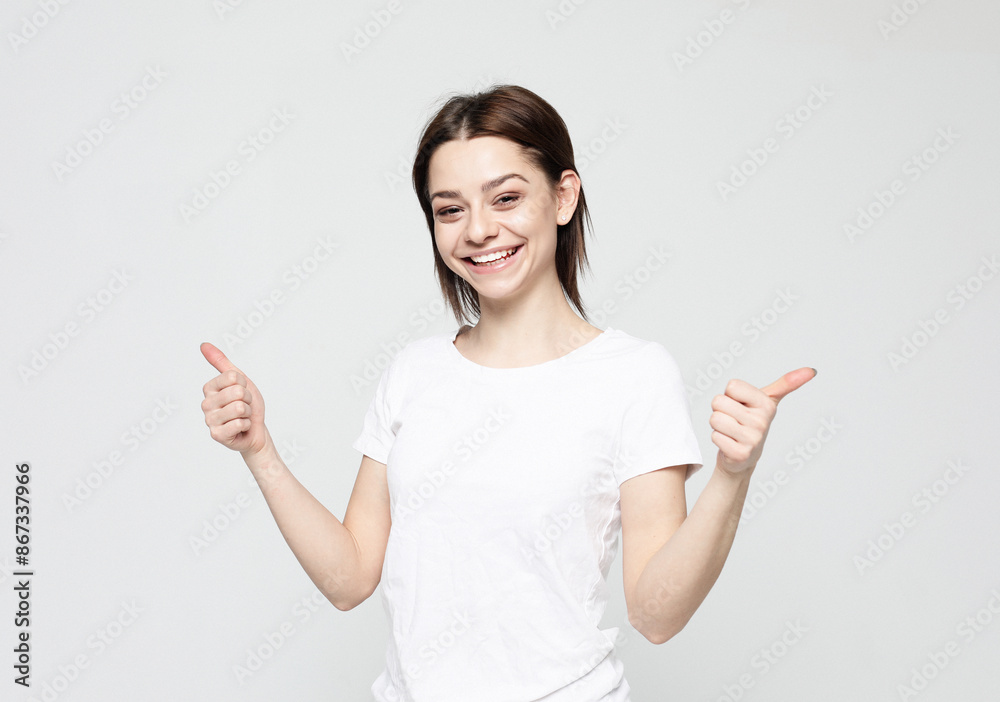 Successful young woman gives thumbs up with two hands over grey background. Successful young woman gives thumbs up with two hands over grey background.