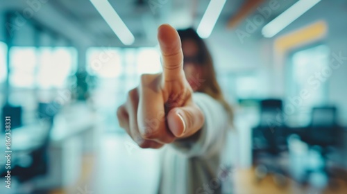 Finger pointing directly at the camera with the person pointing blurred in background standing at a white office