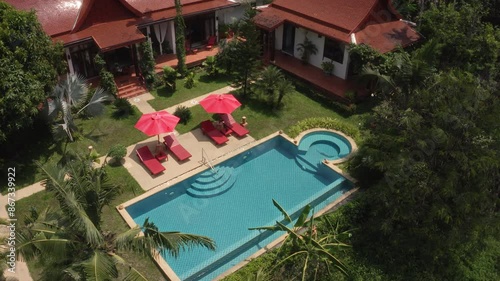 A beautiful aerial view of a tropical villa with red roofs, a swimming pool, and lush gardens