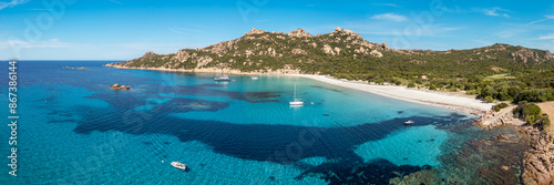 Panoramic aerial view of yachts at Roccapina beach on the Mediterranean coast of Corsica overlooked by the Genoese Tour de Roccapina and Lion of Roccapina, a rocky outcrop in the shape of a lion