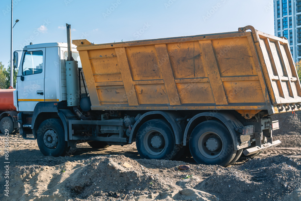 Obraz premium A dump truck at a construction site. Transportation of bulk building materials for use in construction. Self-unloading dump truck. Delivery of construction materials to the construction site.
