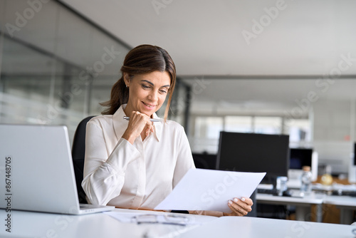 Busy happy mature business woman bank manager working in office checking legal document account invoice in office. Businesswoman of middle age executive, attorney lawyer using laptop at work.