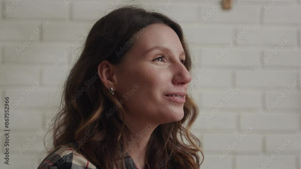A portrait of a joyful woman wearing casual attire in front of a white brick wall