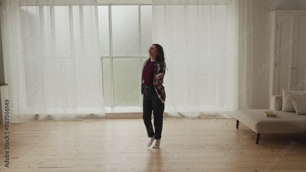 A young woman energetically dancing in a modern living room with white curtains and wooden floors A young woman energetically dancing in a modern living room with white curtains and wooden floors