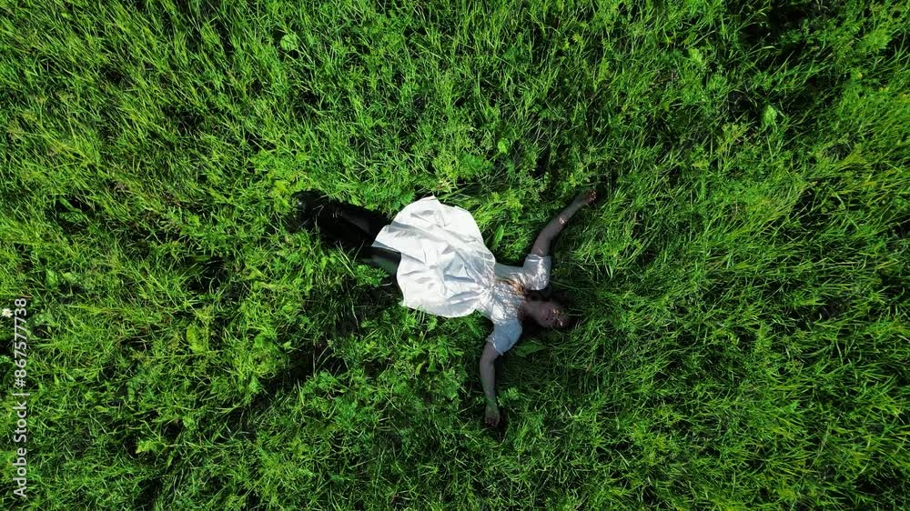 girl in a white dress lies on the green grass - aerial drone video slow motion girl in a white dress lies on the green grass - aerial drone video slow motion