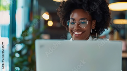 A smiling woman with glasses is using her laptop.