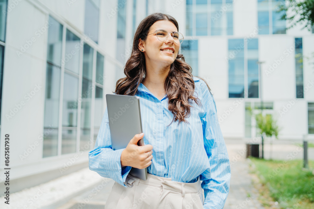 One beautiful young successful business woman going to work at business office modern building while holding laptop and waring glasses One beautiful young successful business woman going to work at business office modern building while holding laptop and waring glasses