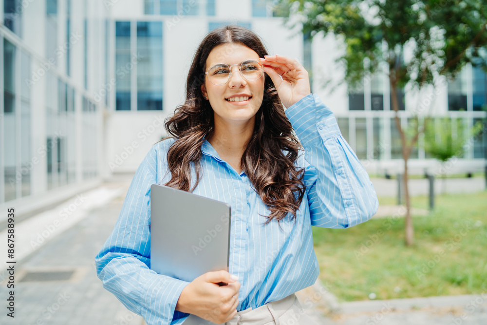 Fototapeta premium One beautiful young successful business woman going to work at business office modern building while holding laptop and waring glasses
