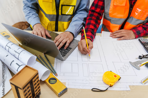 Two men, including a male Asian construction contractor engineer, discuss structural plans and engineering concrete columns and beams of a new house at a desk with a building tower model. photo