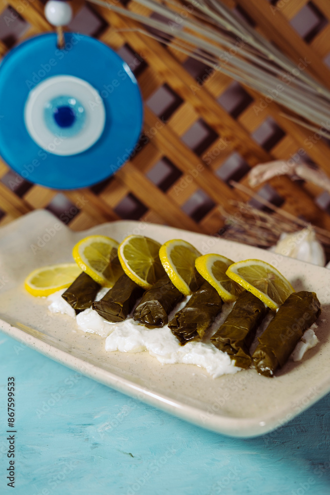 dolma or dolmades greek and turkish national food of stuffed vine grape leaves rolls ooked in olive oil served on blue background with youghurt and lemons dolma or dolmades greek and turkish national food of stuffed vine grape leaves rolls ooked in olive oil served on blue background with youghurt and lemons