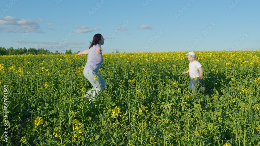 Young Mother With Son Enjoy Playing With His Mom In Yellow Rapeseed Field Countryside. Happy Little Boy With Hat. Countryside. Young Mother With Son Enjoy Playing With His Mom In Yellow Rapeseed Field Countryside. Happy Little Boy With Hat. Countryside.