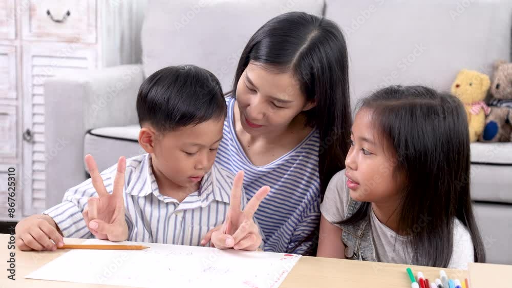 Cheerful Asian mother spend time with two sibling kids teaching homework drawing picture together in living room at home, free time children on holiday bonding happy relationship with mom parenthood Cheerful Asian mother spend time with two sibling kids teaching homework drawing picture together in living room at home, free time children on holiday bonding happy relationship with mom parenthood